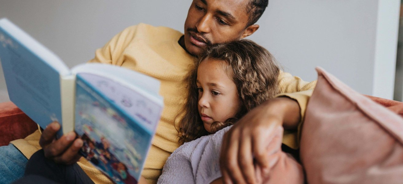 Father reading book with daughter while sitting at home