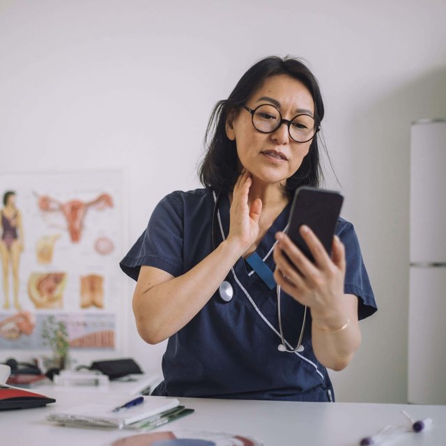 Female otolaryngologist doing online consultation through mobile phone while sitting at desk in medical clinic