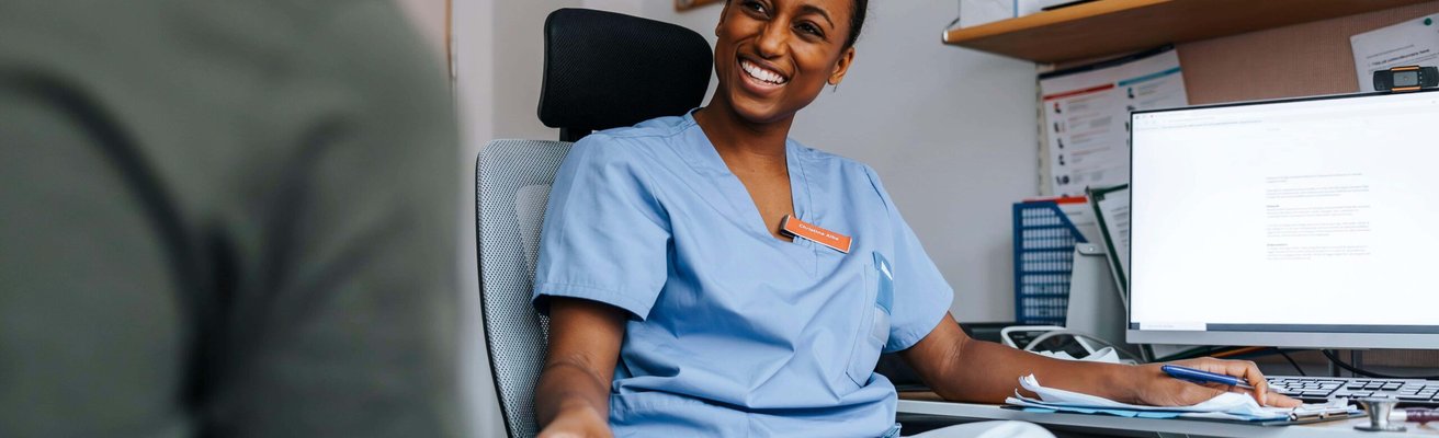 Smiling young medical expert sitting near computer and talking with patient in doctor's office