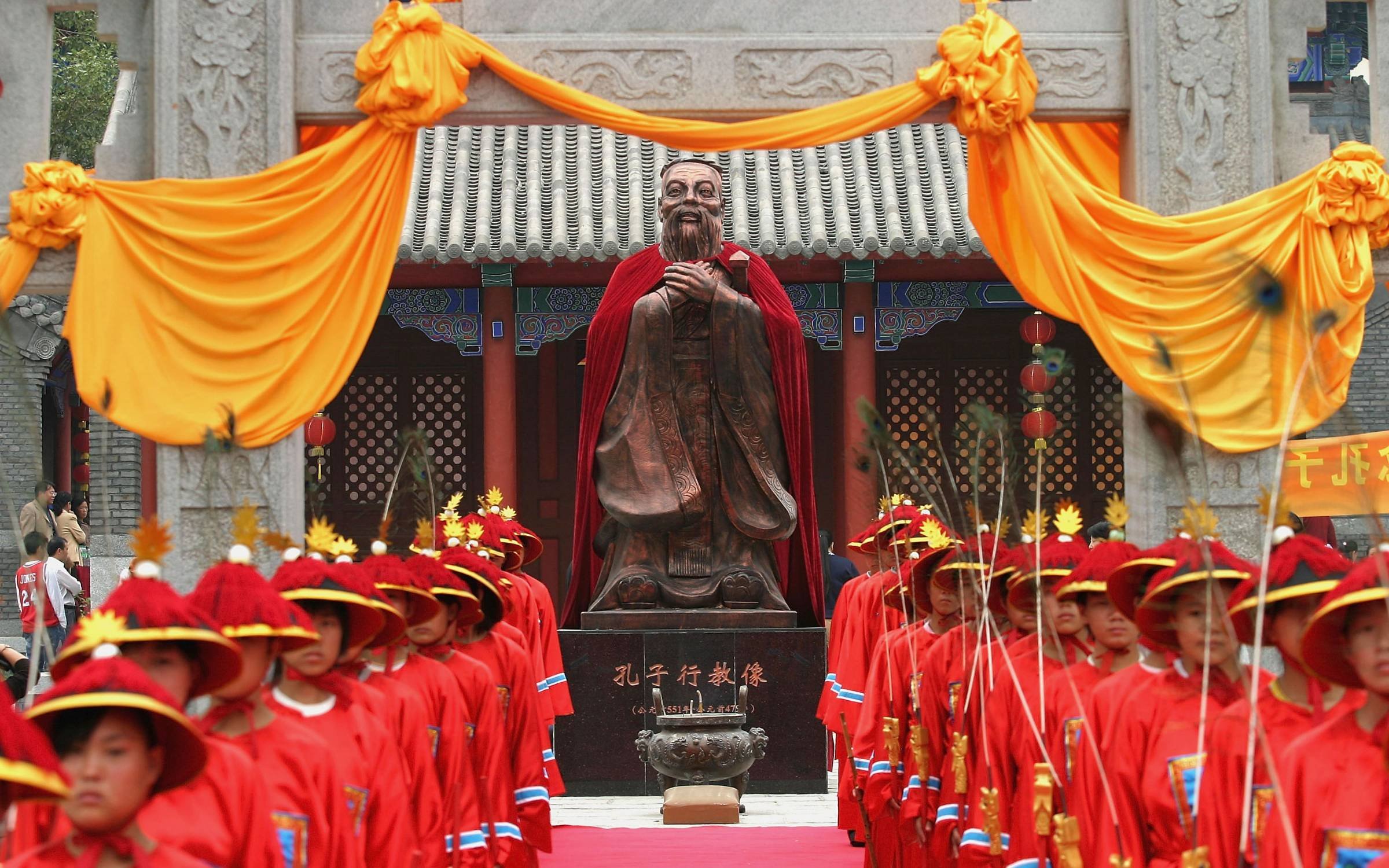 Students dressed in ancient clothes stand in front of the statue of Confucius