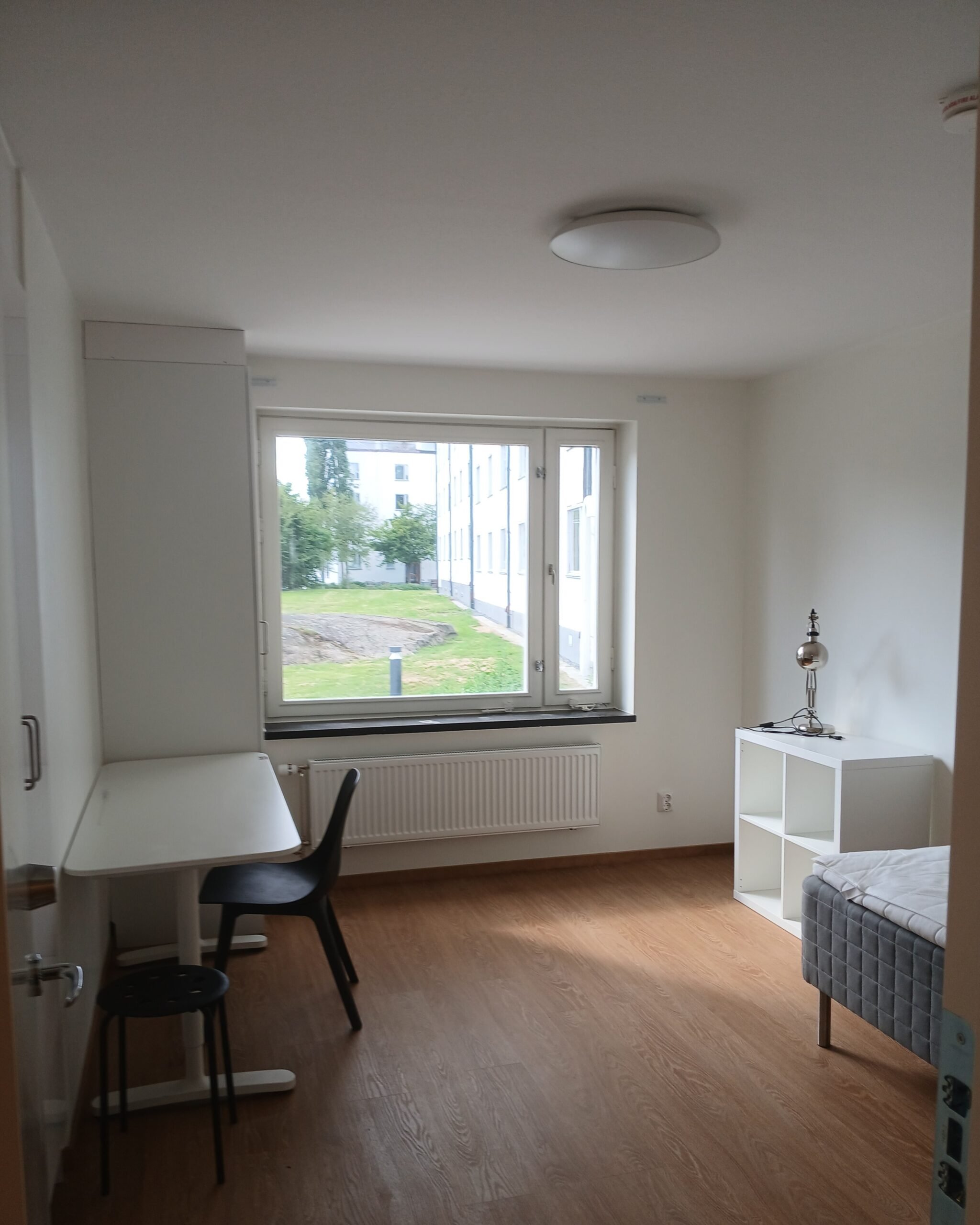 Studentroom with window, desk, chair, storage unit and bed.