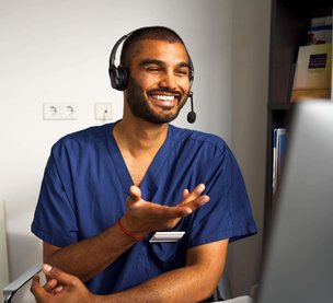 Happy male medical professional wearing headset assisting patient through video call in clinic at hospital