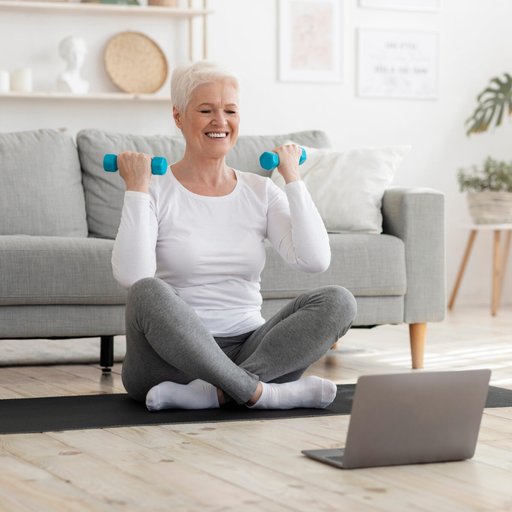 Sporty,Elderly,Lady,Training,At,Home,With,Dumbbells,,Watching,Online