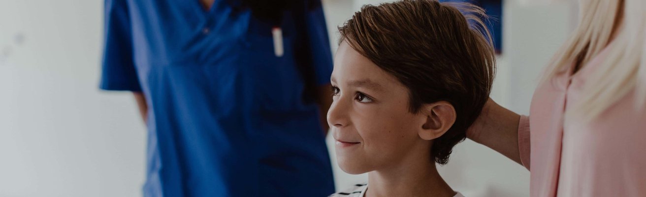 Smiling boy standing by mother while female nurse