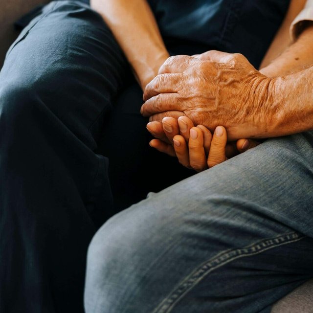 Midsection of senior male holding hands of female caregiver while sitting on sofa at nursing home