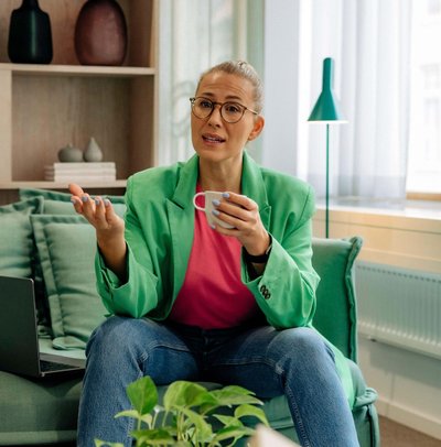 Mature female boss talking and holding cup while sitting on sofa at home