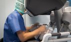 A surgeon manipulates the controls of a robot that operates on a patient.