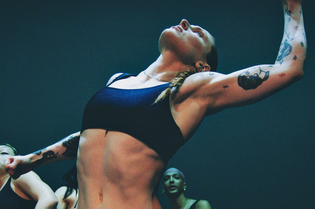 Dansare lutar huvudet bakåt med armarna utsträckta, i ett kraftfullt sceniskt ögonblick.