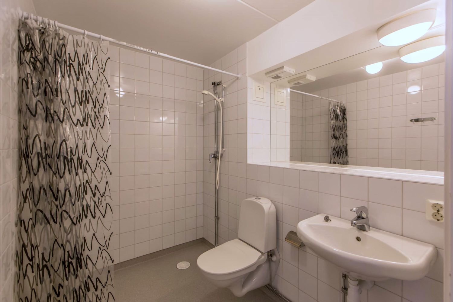 White, tiled bathroom with wc, sink and shower.