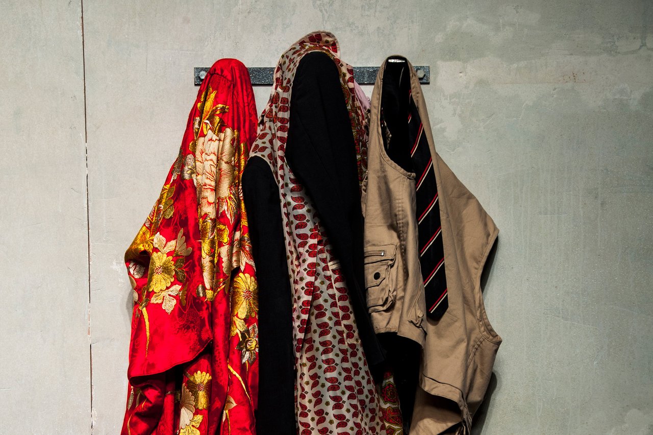 En vit vägg med tre krokar där det hänger kläder.