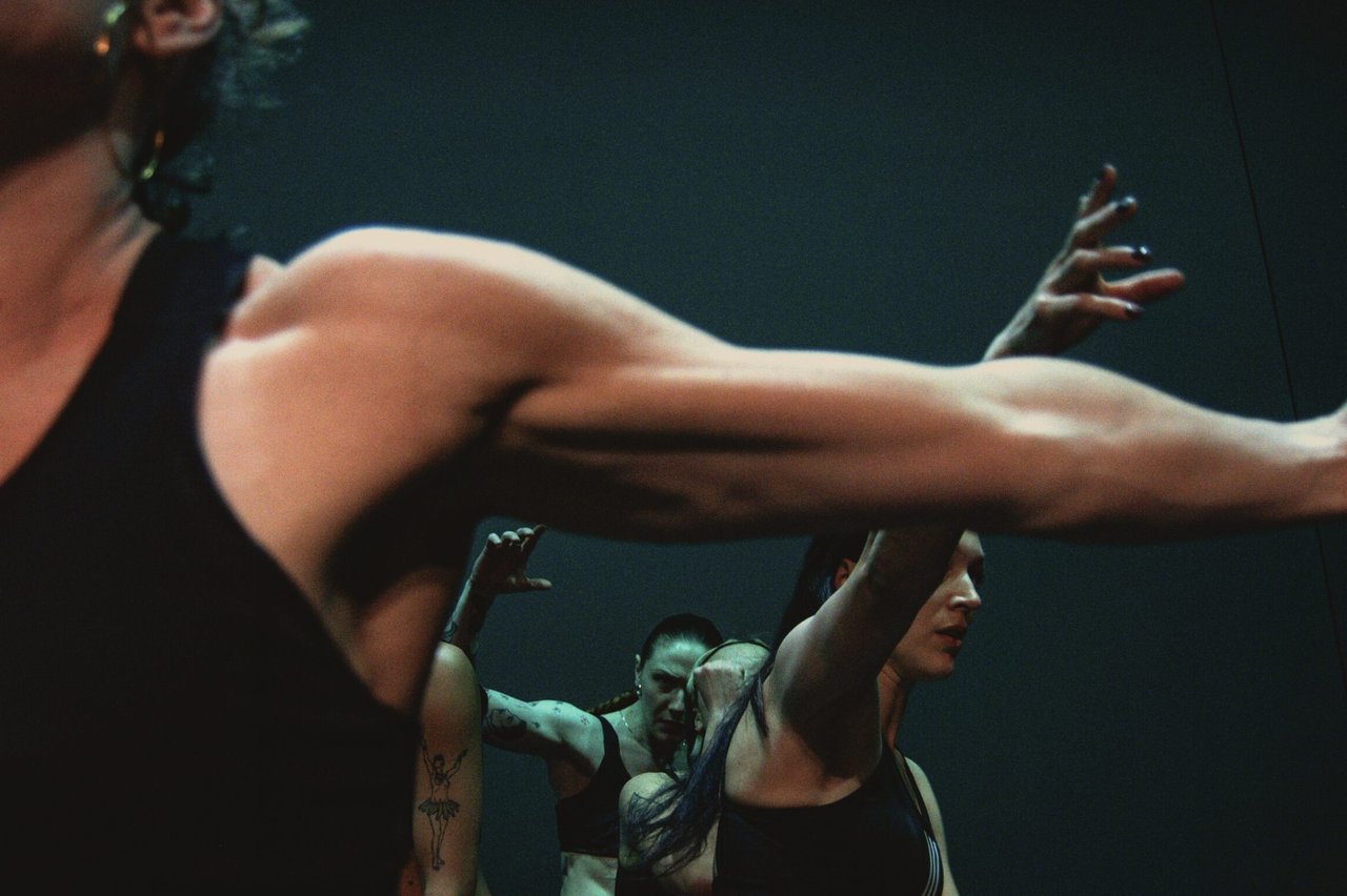 Närbild av dansares armar i rörelse, med fler kroppar i bakgrunden i samma koreografi.