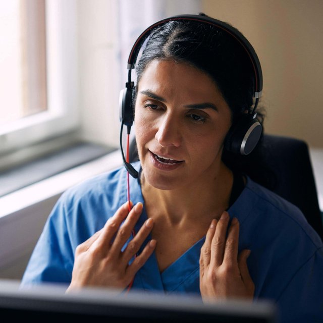 Female doctor wearing headset and having discussion over video call in clinic