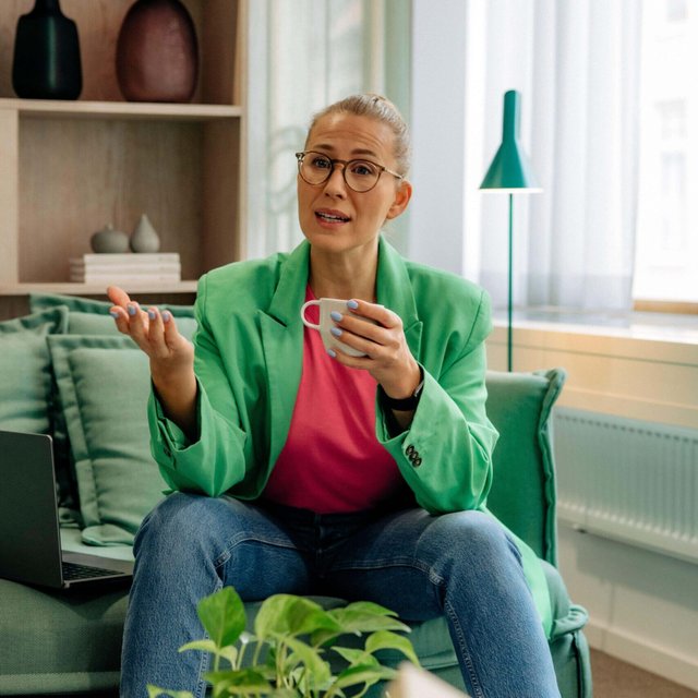 Mature female boss talking and holding cup while sitting on sofa at home