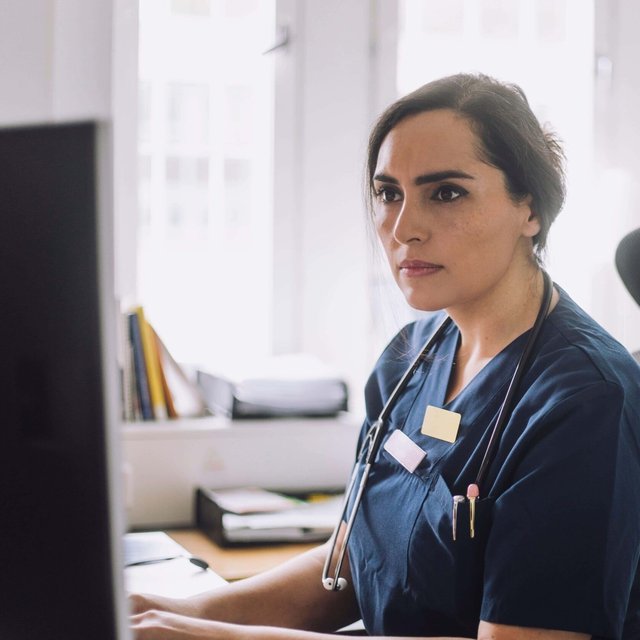 Focused female nurse working while sitting on chair in clinic