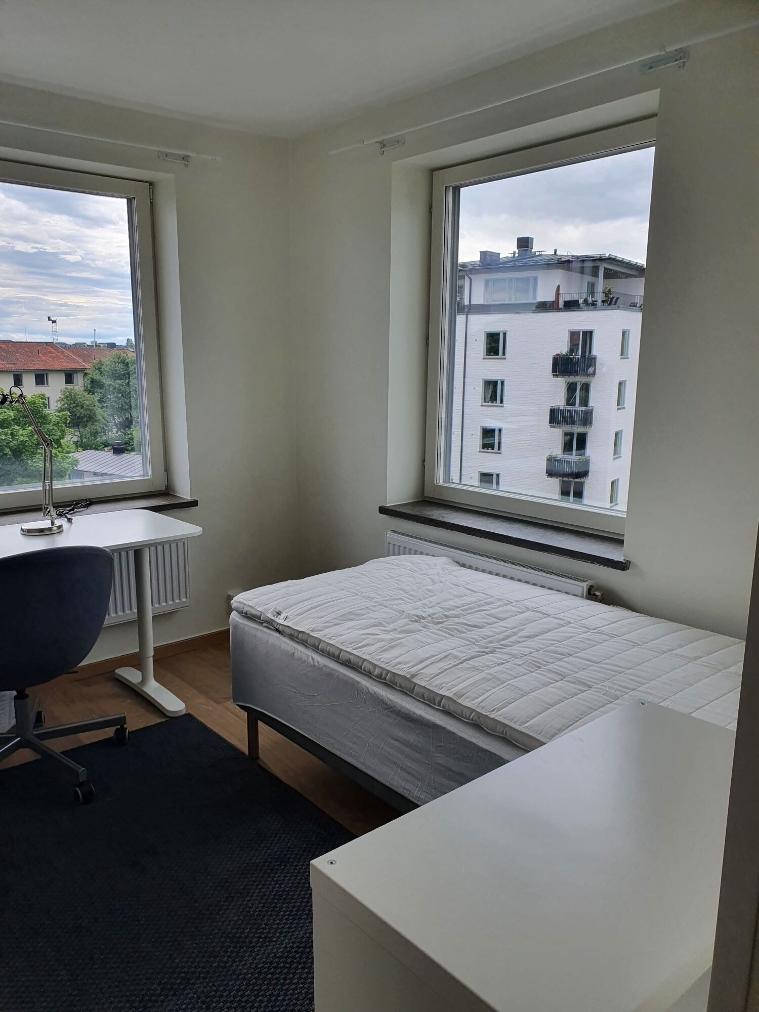 corner room with two windows, bed, desk and chair.