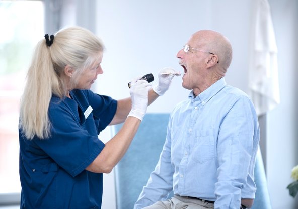Kvinnlig läkare tittar i svalget på äldre manlig patient.