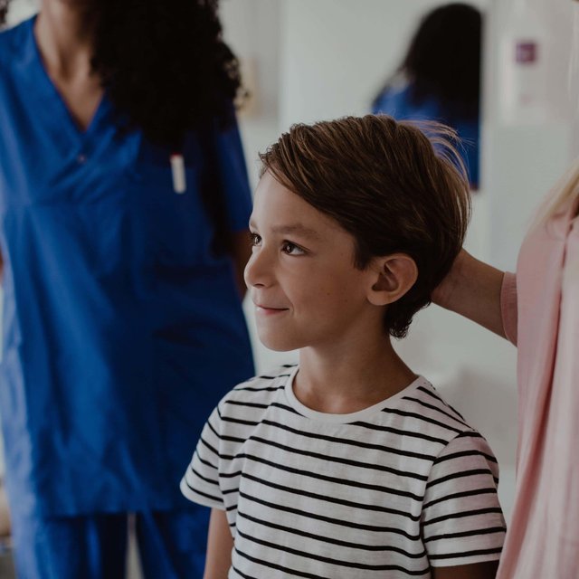 Smiling boy standing by mother while female nurse