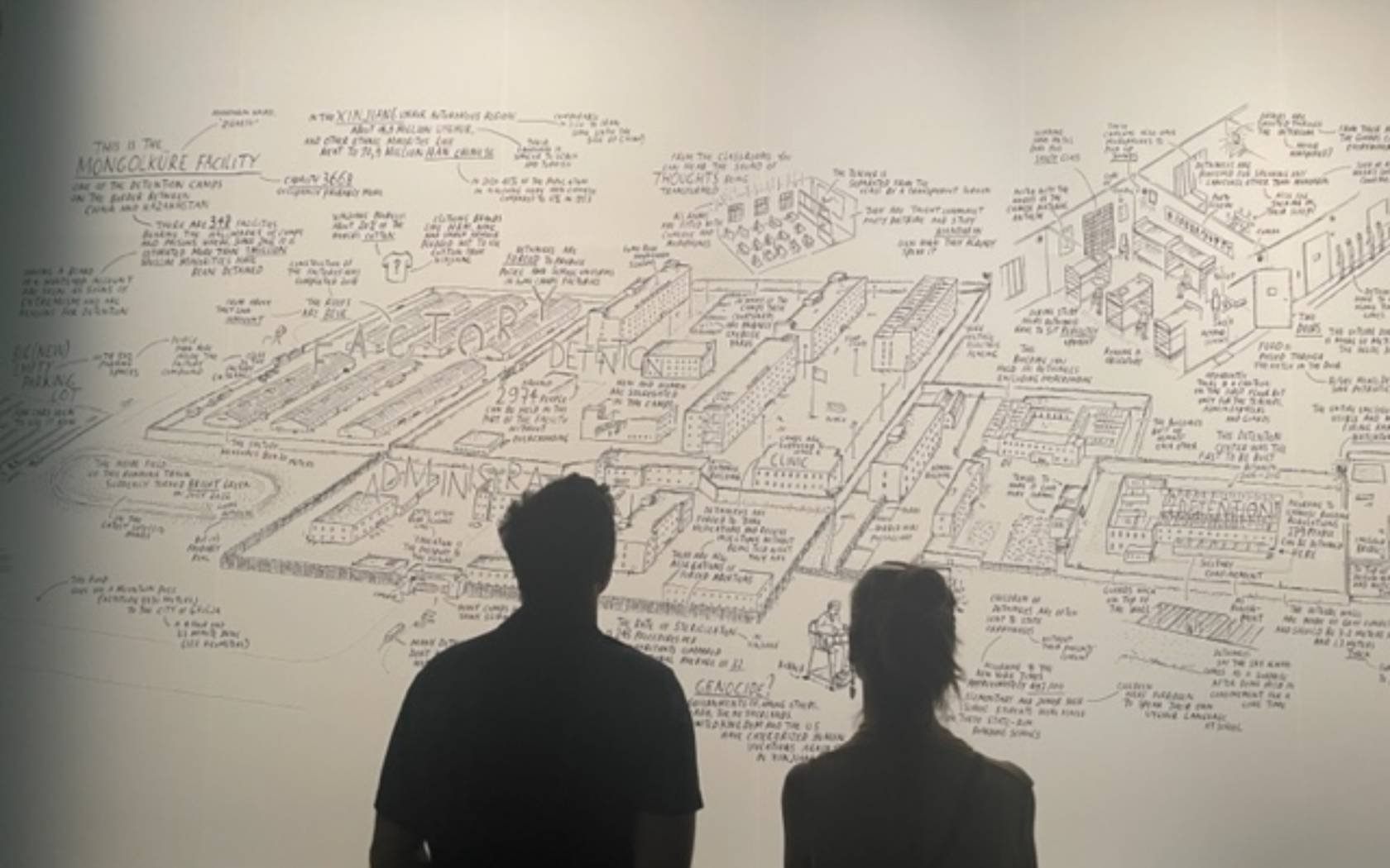 Two visitors look at a giant cartoon mural depicting a detention camp in the Chinese region of Xinjiang at the Venice Architecture Biennale.