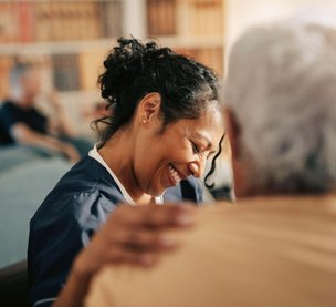 Smiling female nursing assistant with hand on shoulder of senior patient at retirement home
