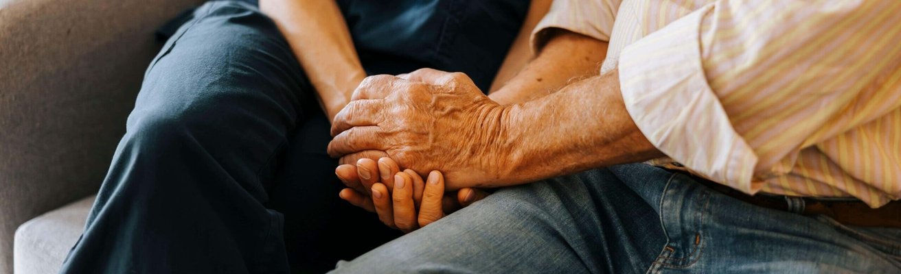 Midsection of senior male holding hands of female caregiver while sitting on sofa at nursing home