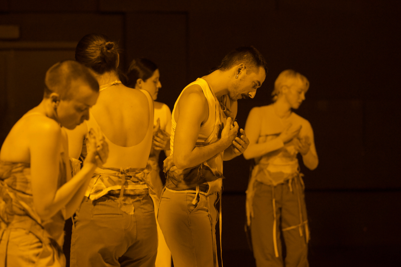 Dansarna tittar ner på sina händer medan de rör sig över scenen.