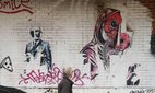 A man walks past mural which connects gas masks and the Covid pandemic.