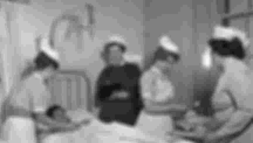 Nurses and matron gathered around a patient in hospital, c. 1960. M&N / Alamy Stock Photo