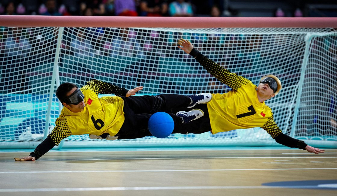 Två målvakter i goalball slänger sig åt varsitt håll och räddar bollen.
