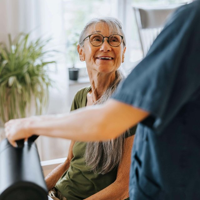 Smiling senior woman sitting at dining table and talking with nurse at care home