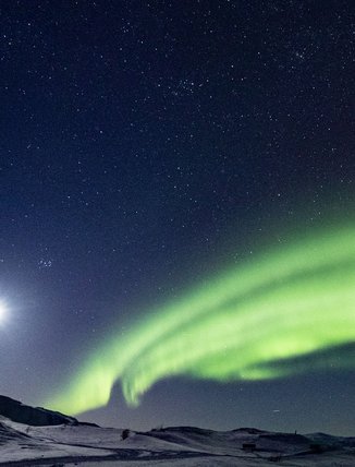 The Northern Lights and a full moon high up on the bare mountain