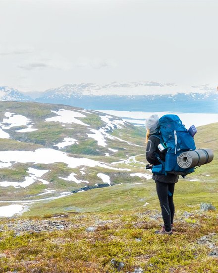 woman looking at the view of snow-covered mountain peaks in early summer
