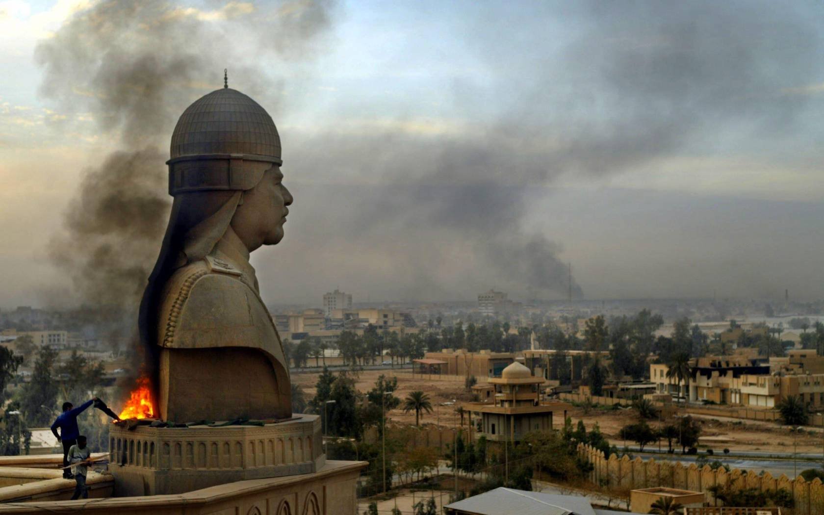 Iraqi protestors set a fire at the base of a statue of Saddam Hussein, April 2003.