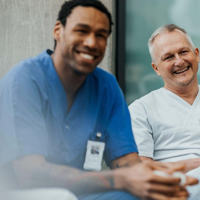 Happy mature male physician sitting with team in clinic
