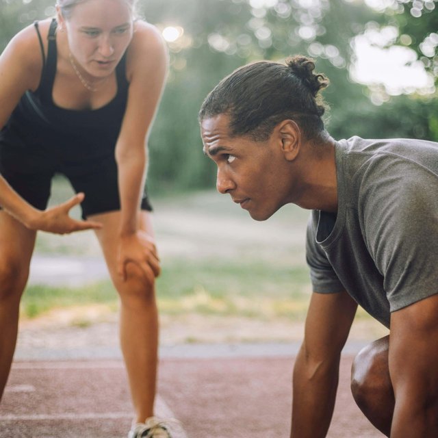 Female instructor guiding determined man preparing for sprint on running track
