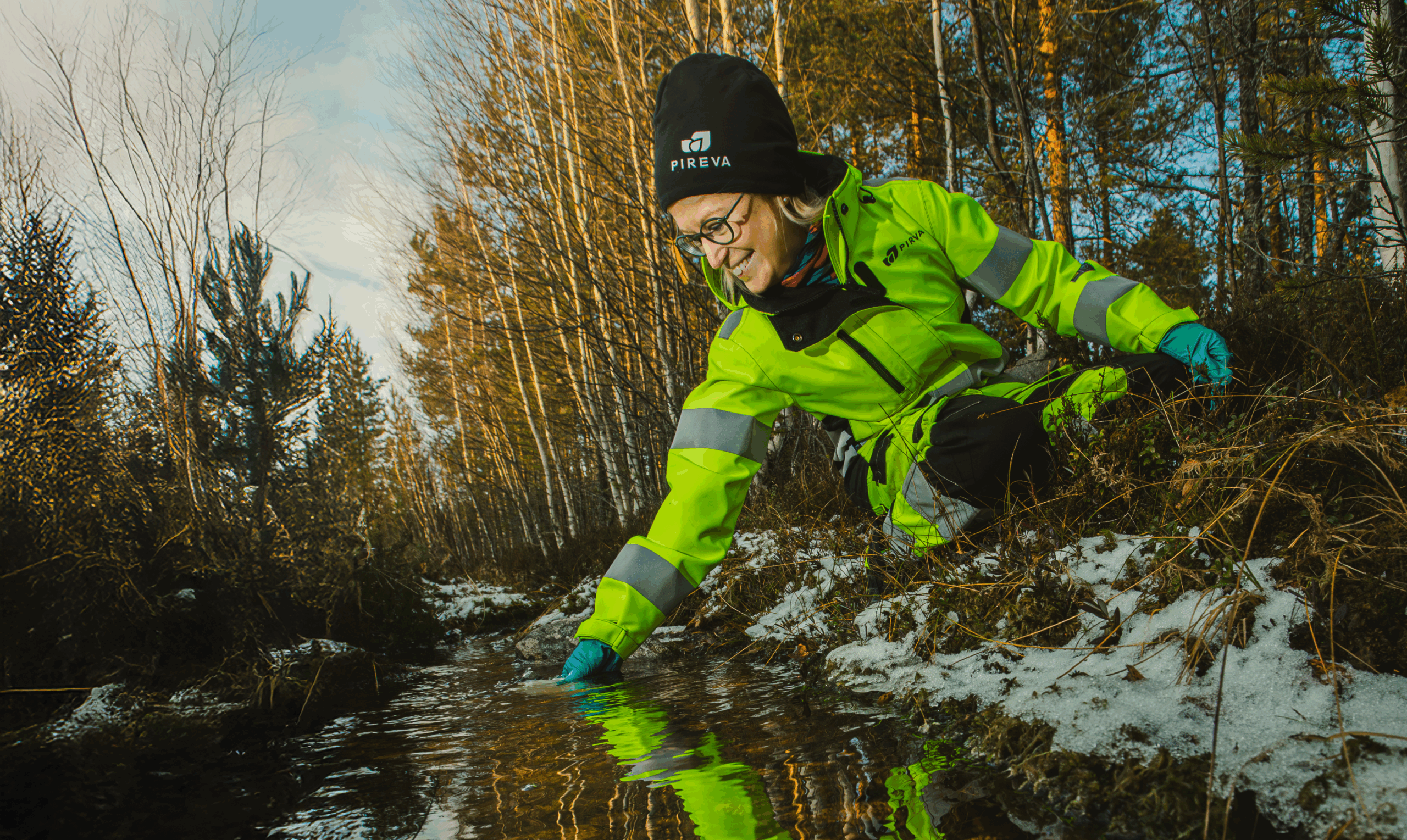 Medarbetare tar vattenprov i ett vattendrag i skogsmilj&ouml;.
