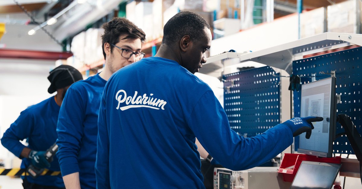 One Polarium employee shows another what is on the screen in front of them. A third employee can be seen behind them. They are all wearing blue shirts with the Polarium logo on the back.
