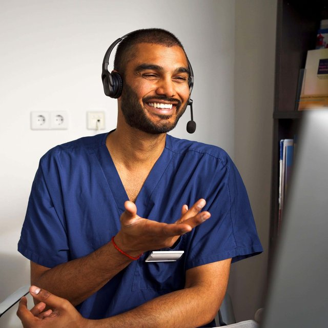 Happy male medical professional wearing headset assisting patient through video call in clinic at hospital