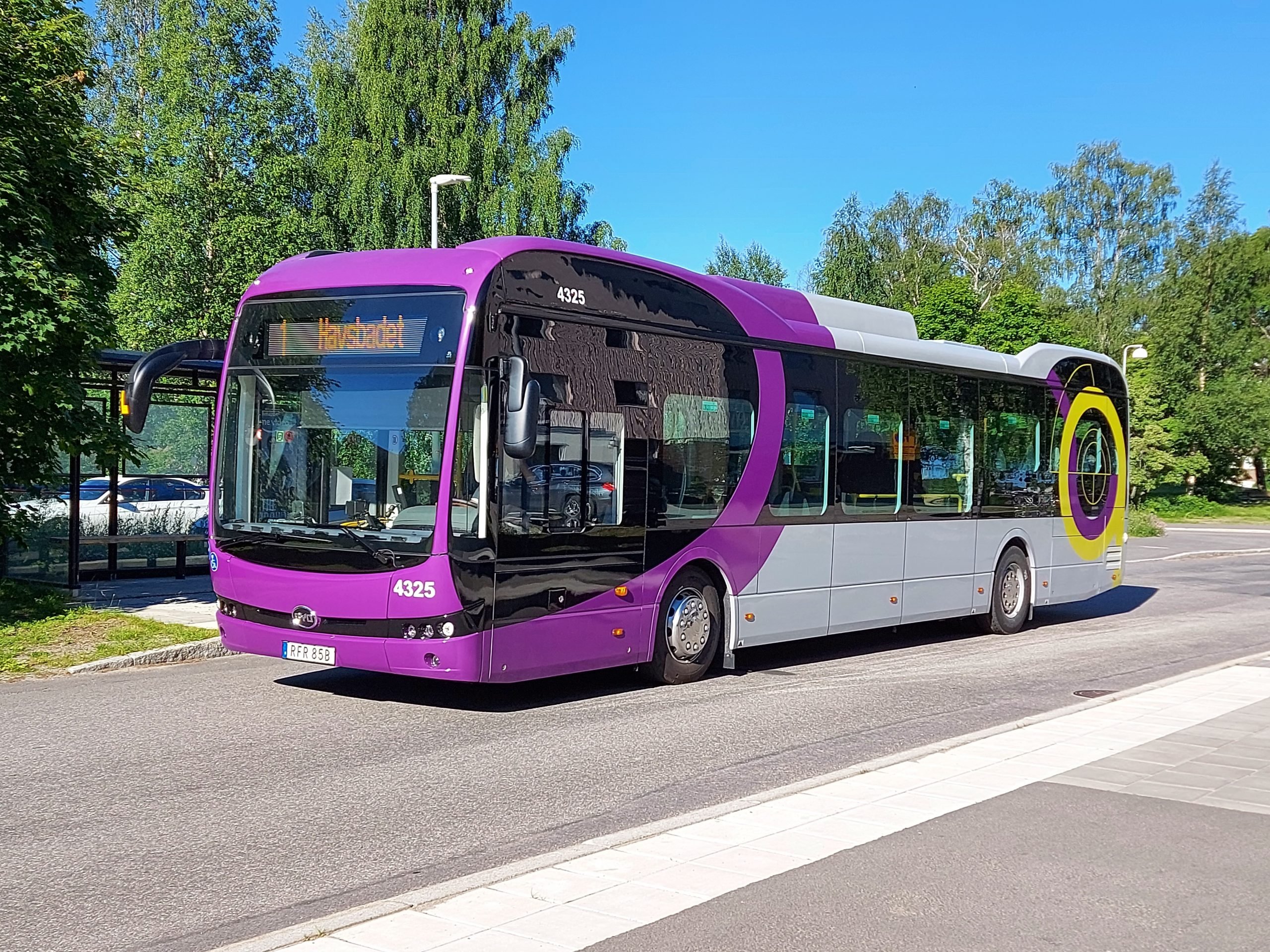 En lila och grå elbuss står på en parkering