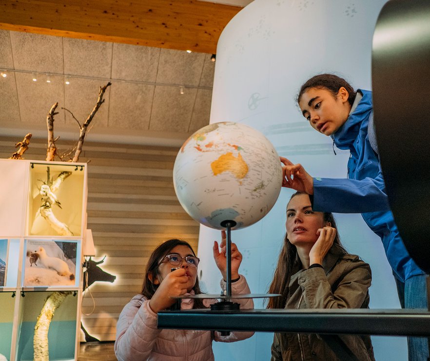 tv&aring; flickor och deras mamma kollar p&aring; en jordglob p&aring; naturum i Abisko