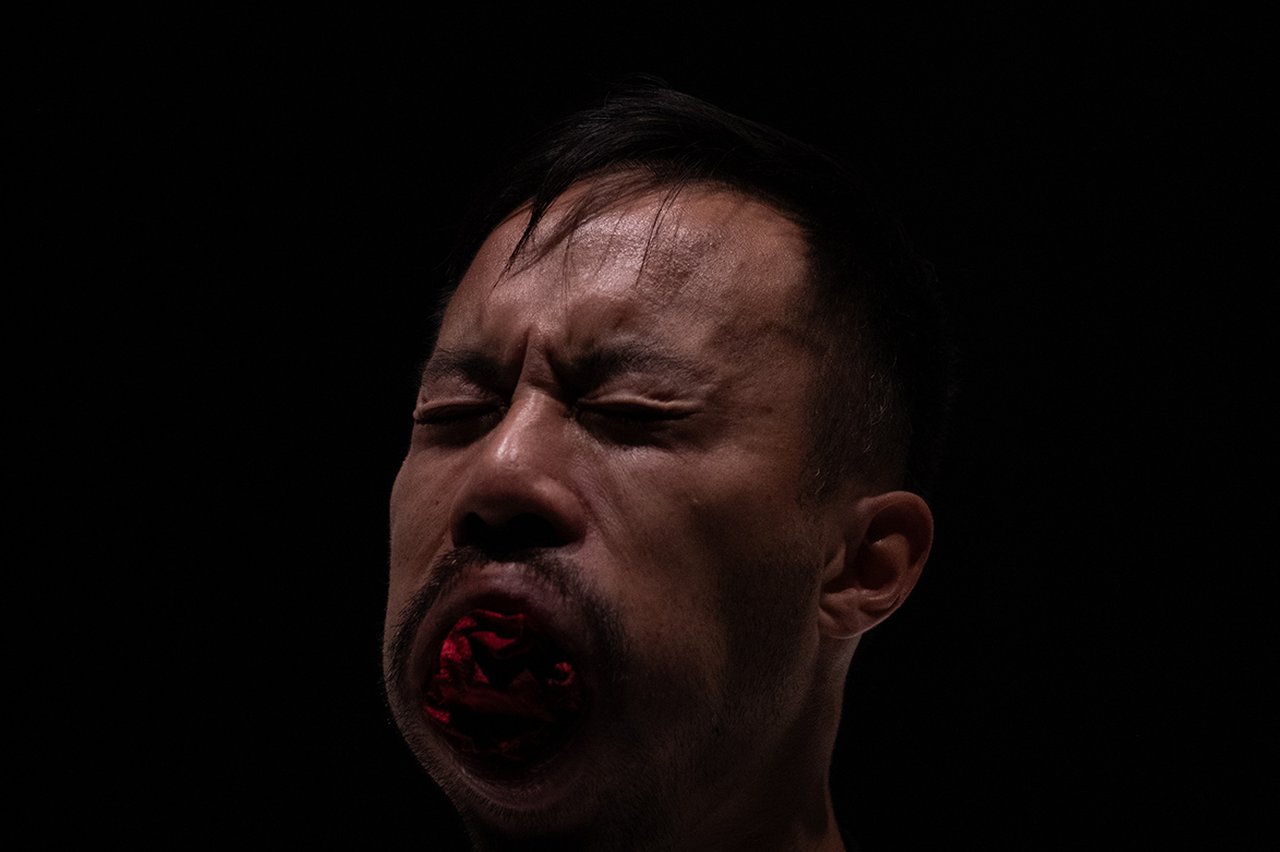 Närbild av en man mot svart bakgrund med slutna ögon och munnen öppen i ett starkt, intensivt uttryck.