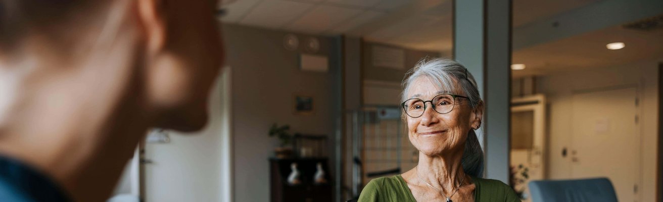 Smiling senior woman sitting in wheelchair and getting consoled by female caregiver at care home