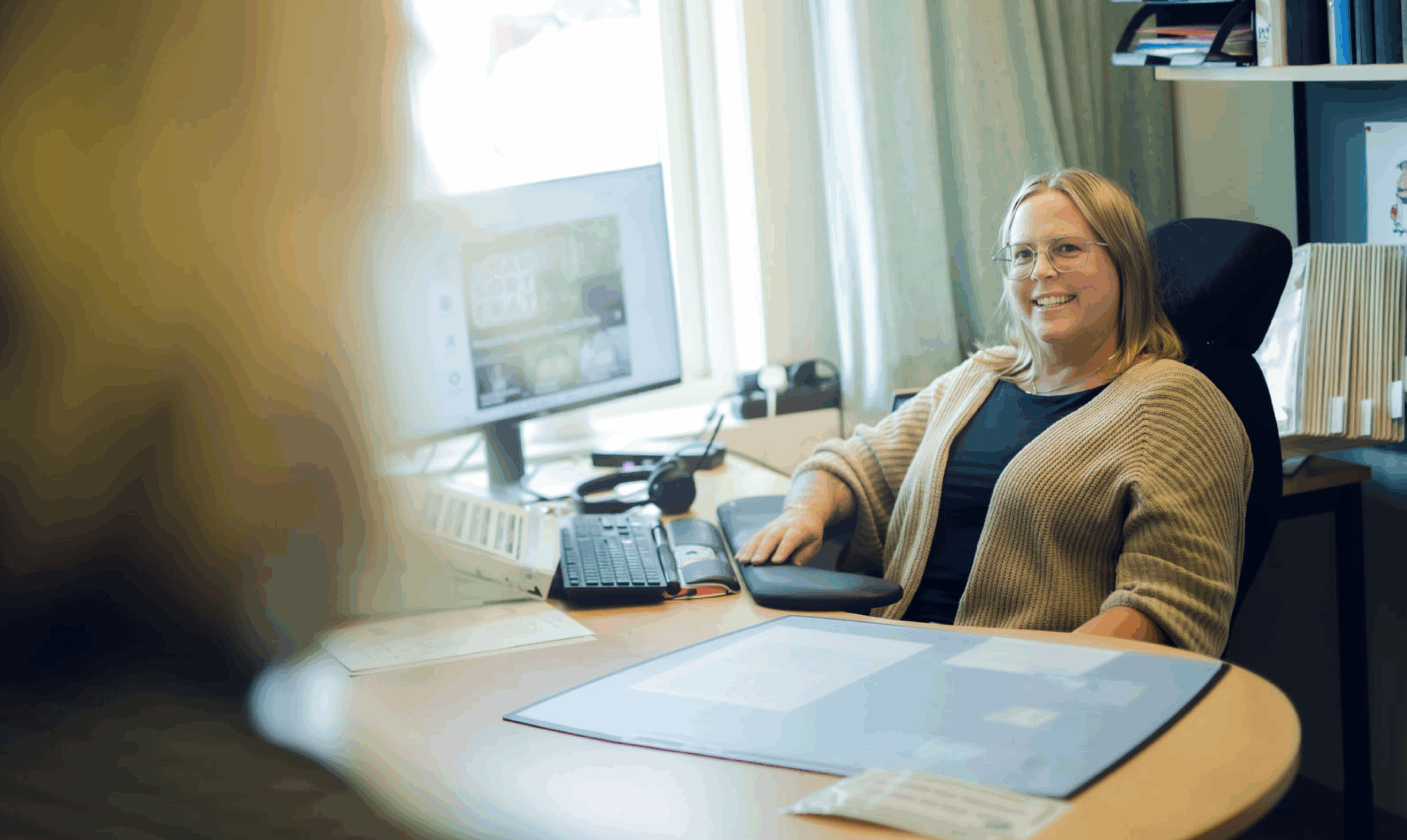 Projektledare sitter vid skrivbord med dator och arbetar med dokument i ett kontor.