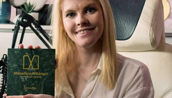 Emma Bliss sitter i en gamingstol och håller upp priset för månadens Nätängel.