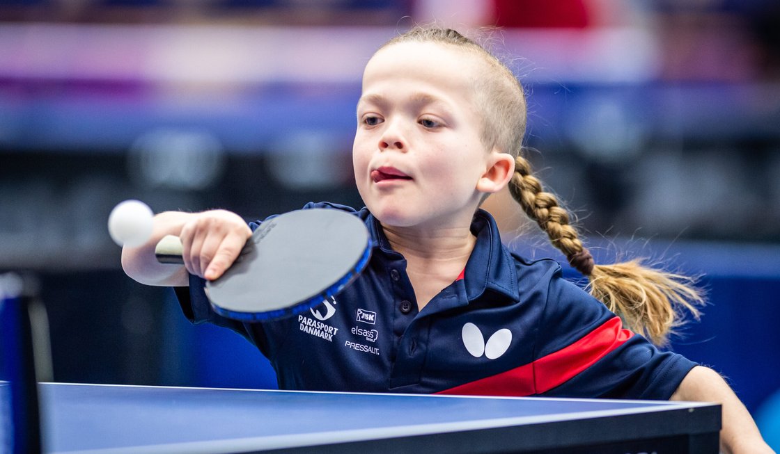 Flicka med lång fläta slår en backhand i bordtennis.