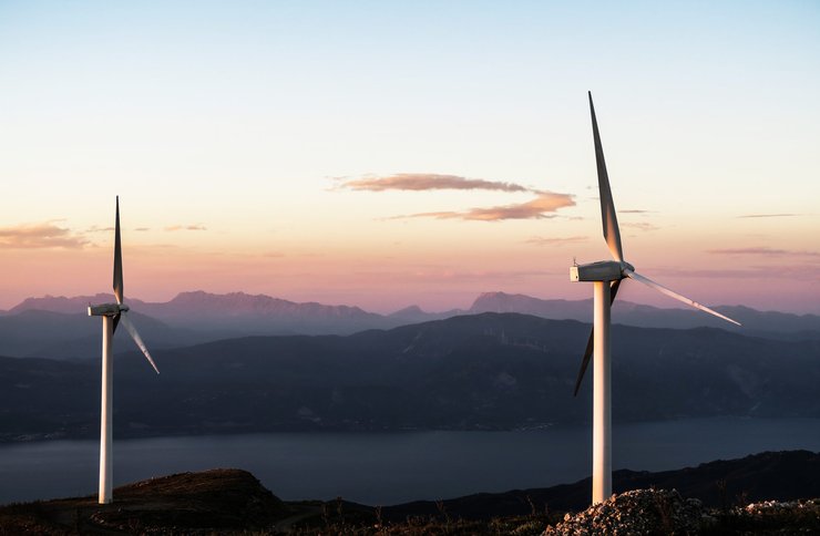 Two wind turbines stand out in front of a beautiful background of mountains during sunset.