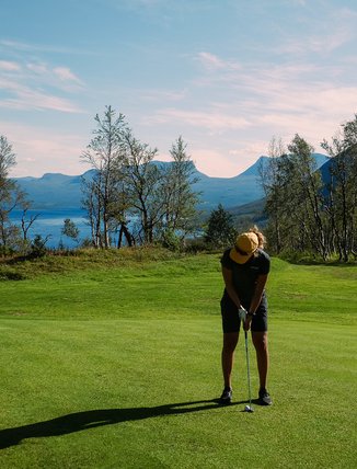 kvinna m&aring;ttar med sin putter p&aring; golfbanan en solig dag med Lapporten i bakgrunden
