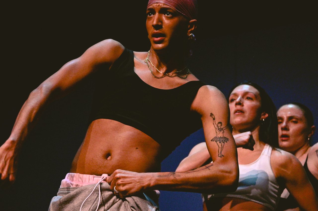 Dansare i förgrunden med spänd kroppshållning, med två andra dansare tätt bakom.