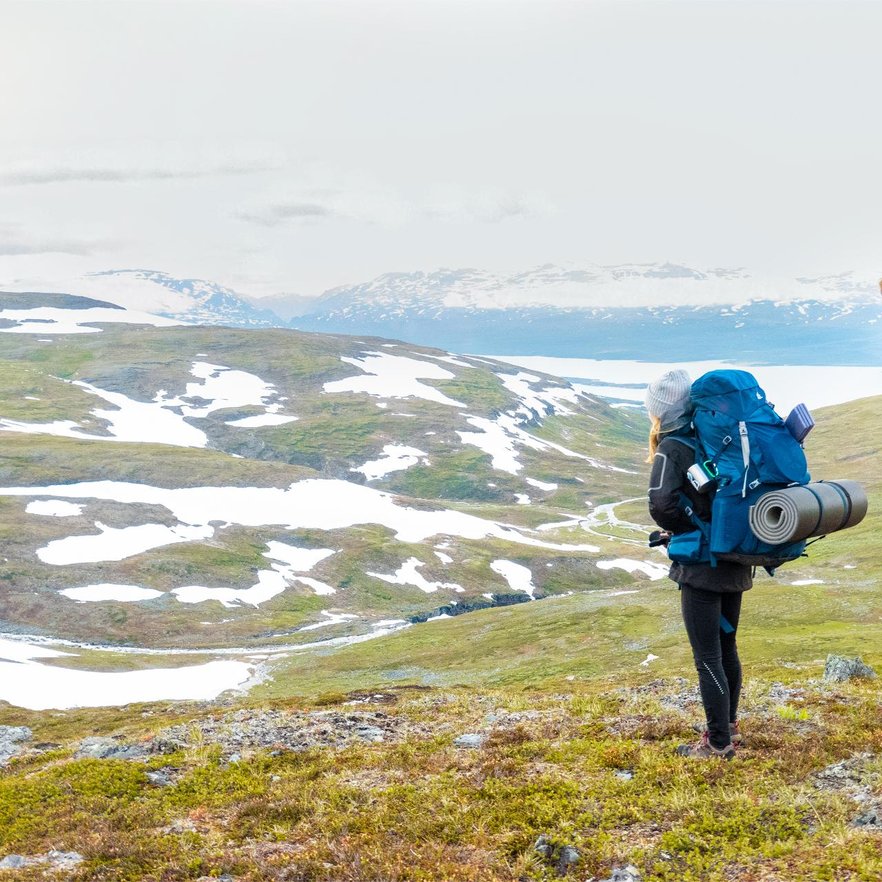 kvinna kollar p&aring; utsikten av sn&ouml;t&auml;cka fj&auml;lltoppar under f&ouml;rsommaren