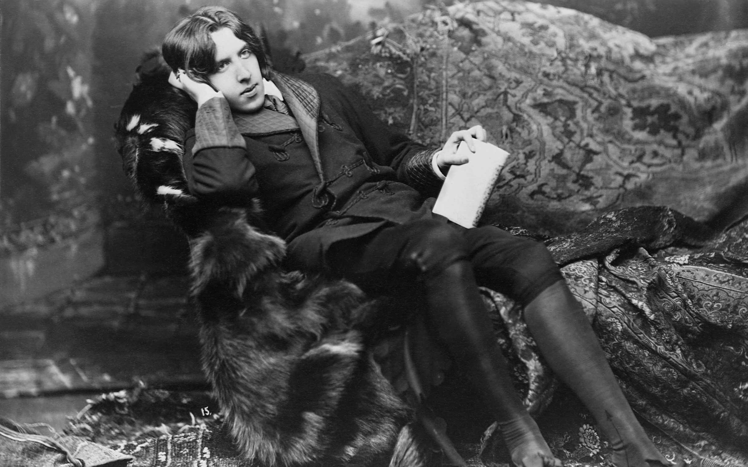 Poet and novelist, Oscar Wilde, (1854-1900), in his typical costume of a velvet robe and black silk stockings. Wilde was one of the leading dandies of the Victorian era