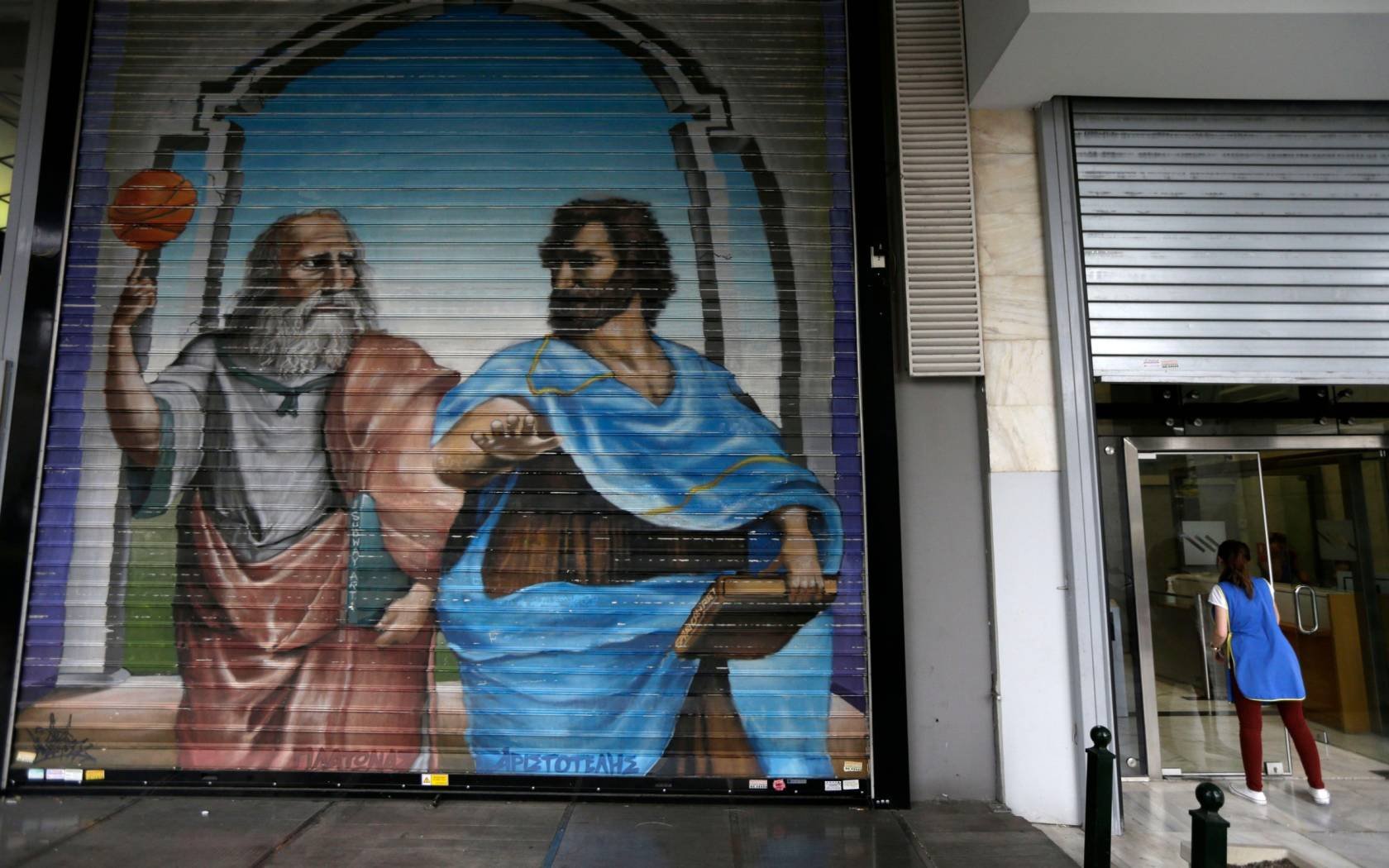 A woman cleans the window of a bank next to graffiti of Plato and Aristotle in Greece during the Eurozone Crisis.